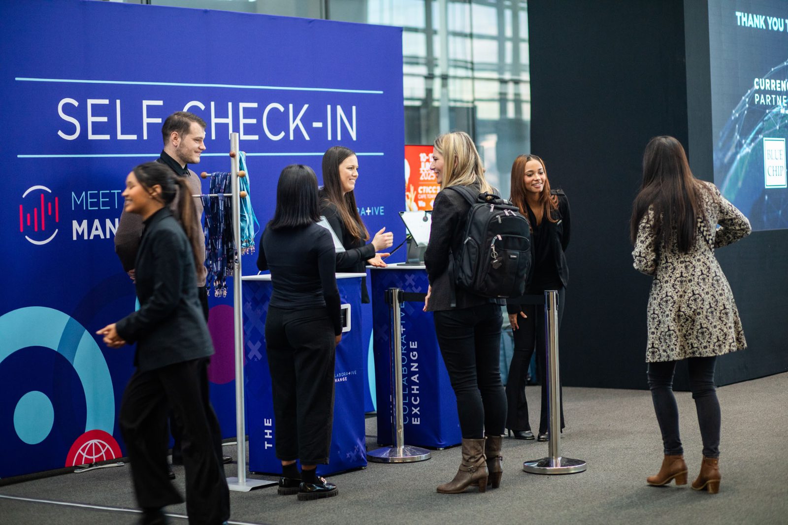 Guests at a GEL self check-in stand being helped by staff